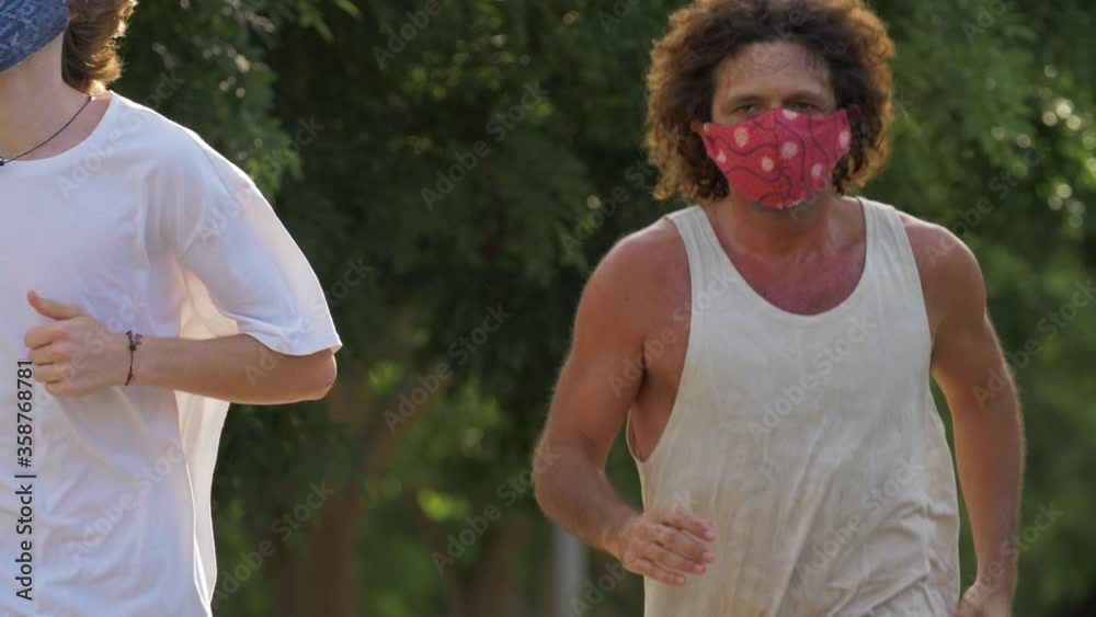 Male friends running in a Park. Covering their face with colorful homemade fabric masks. Covid 19. Coronavirus protection Male friends running in a Park. Covering their face with colorful homemade fabric masks. Covid 19. Coronavirus protection