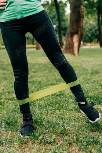 Cropped view of sportswoman using resistance band while training in park