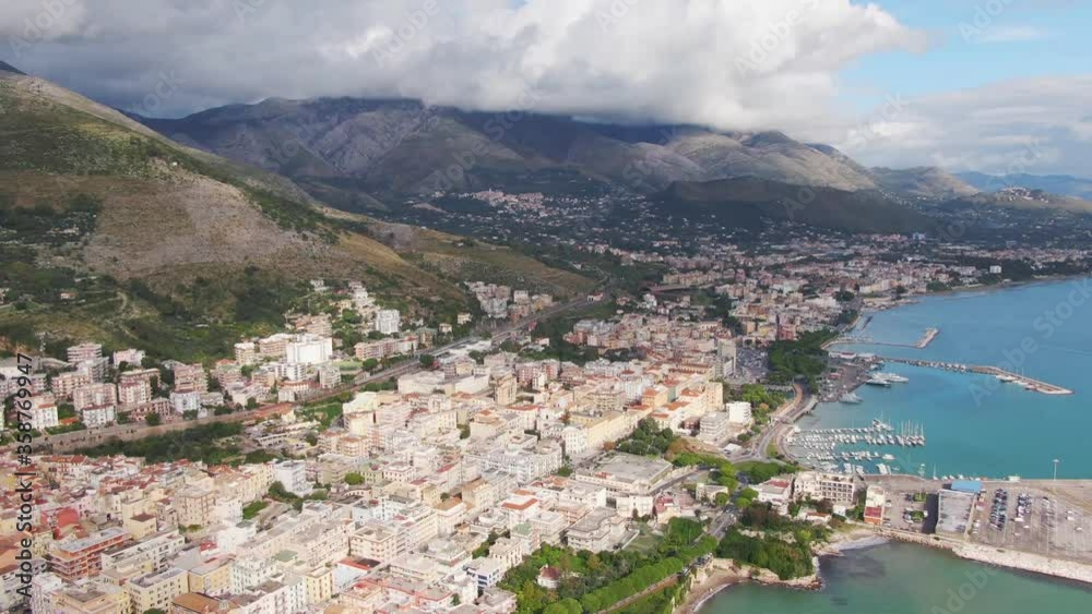 Overhead flight of urban downtown Gaeta city, buildings, boats docked at seaport marina with mountain ranges in background, Italy, aerial pan left Overhead flight of urban downtown Gaeta city, buildings, boats docked at seaport marina with mountain ranges in background, Italy, aerial pan left