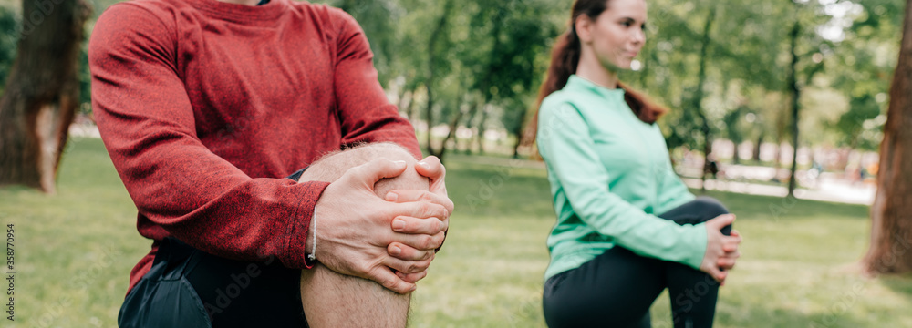 Selective focus of young couple stretching in park, panoramic crop Selective focus of young couple stretching in park, panoramic crop