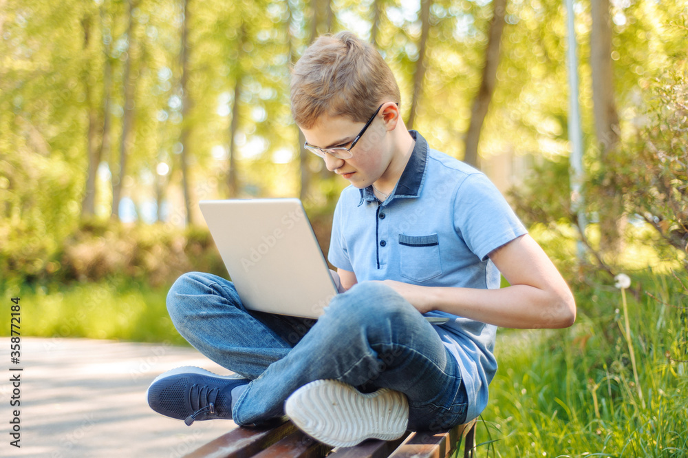 A teenager with a laptop on a park bench. Distance learning. Learn anywhere.