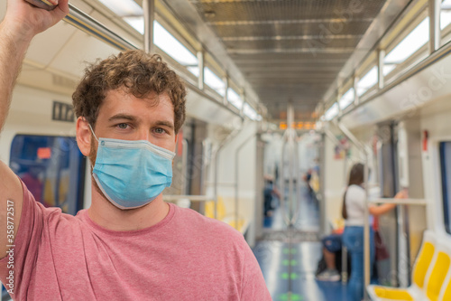 Public transport, portrait young man traveling inside train standing while keeping safety distance and mask, looking straight ahead