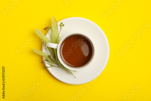 Cup of linden tea on yellow background, top view