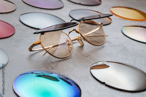 Assortment of different multicolored lenses for eyewear, fashion trendy sunglasses with changeable lenses lying on table in professional optical shop. Optician technician and eyesight concept 