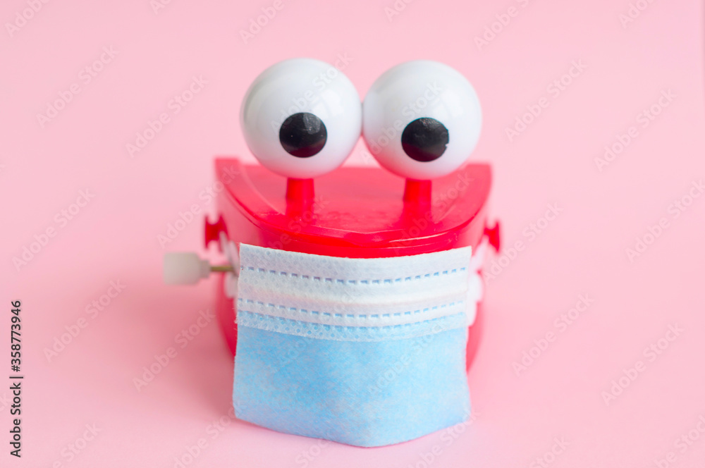 Fototapeta premium toy with smiling teeth and eyes with face mask on pink background as a concept of dentistry and healthy oral cavity and smile during pandemic