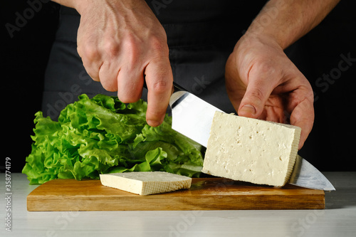 Chef cuts tofu cheese on a wooden board. High quality photo