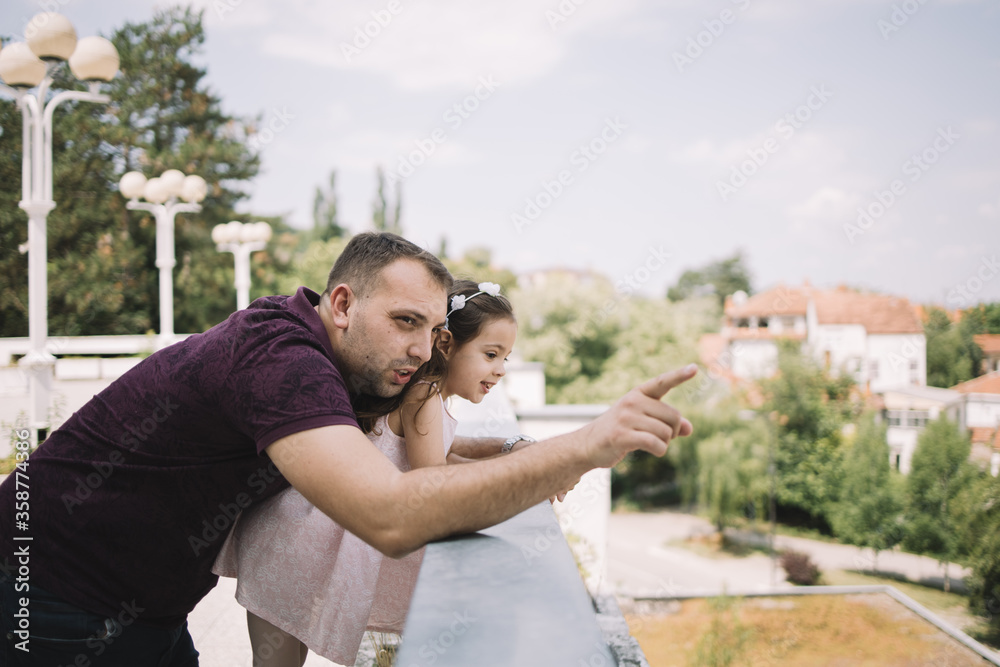 Man hand pointing while hugging his little daughter. Father and daughter leaning on fence and enjoying sunny summer day.