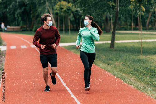 Runners in medical masks looking at each other while training on running track in park