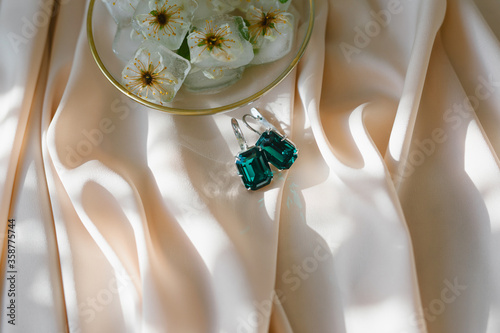 
Ice cubes with flowers and emerald earrings on silk. Fashion photography accessories. The concept of jewelry.