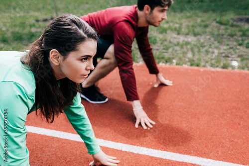 Selective focus of sportswoman standing in starting position near boyfriend on running path