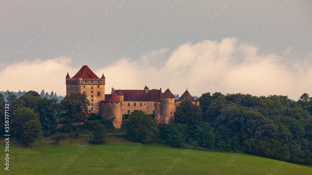 Landscape view with French chateau building in Jura region. House with tower on a hill surrounded by trees scenery.