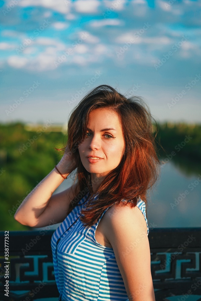 Portrait of a brunette girl with long hair on the background of a panorama of the city from the bridge at sunset