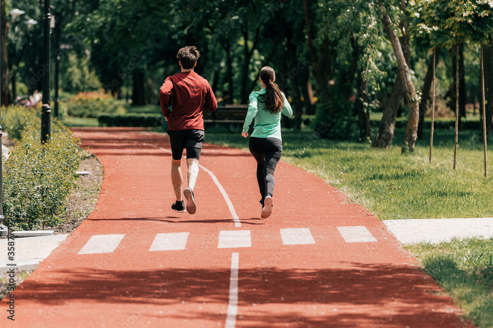 Fototapeta premium Back view of young couple jogging together on running track in park