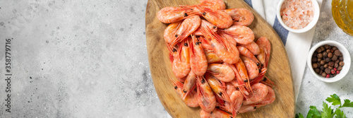Prawns on a wooden Board on the light gray kitchen table. Lots of shrimp on the serving Board. The view from the top. Banner