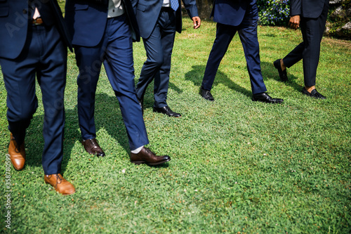 Legs of men in suits walking on the grass.