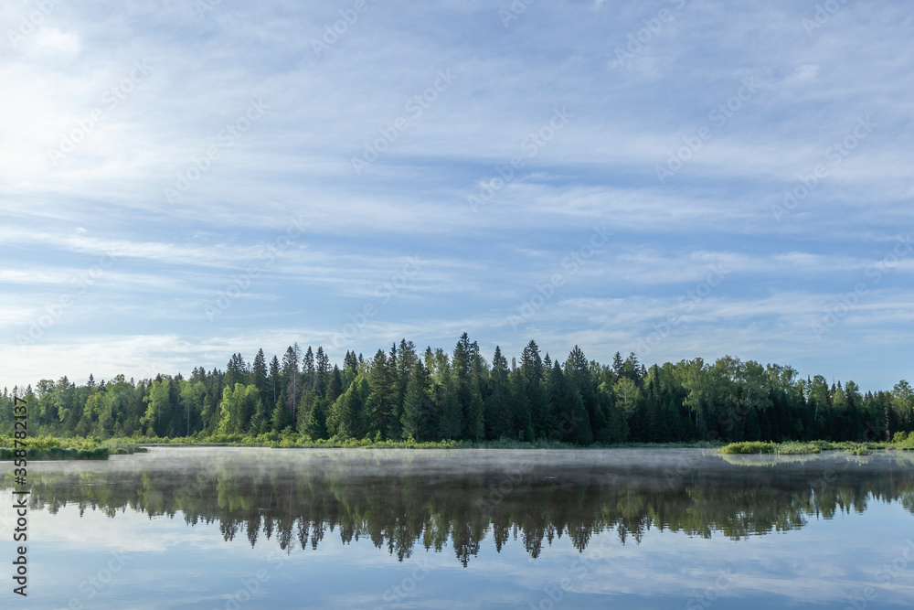 The sky and the forest are reflected in the river.