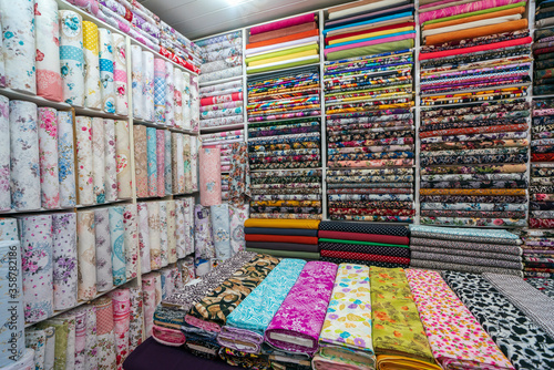Rolls of cotton with colorful and beautiful patterns in the shop selling fabrics as rolls of fabric that are woven with machines in the factory. Floral pattern, various colors fabrics. Linens shop