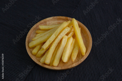 French fries on a wooden plate on a black fabric floor