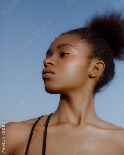 Portrait of dark-skinned young model on background of blue sky with natural make-up