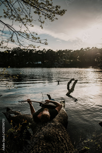 Man playing guitar while lying on tree trunk
