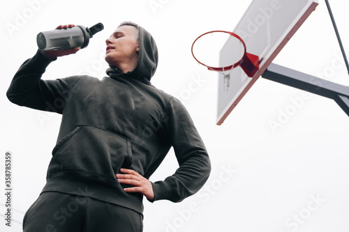 Portrait of a young fitness trainer of a man who in a black tracksuit drinks a pair of pre workouts before training. photo