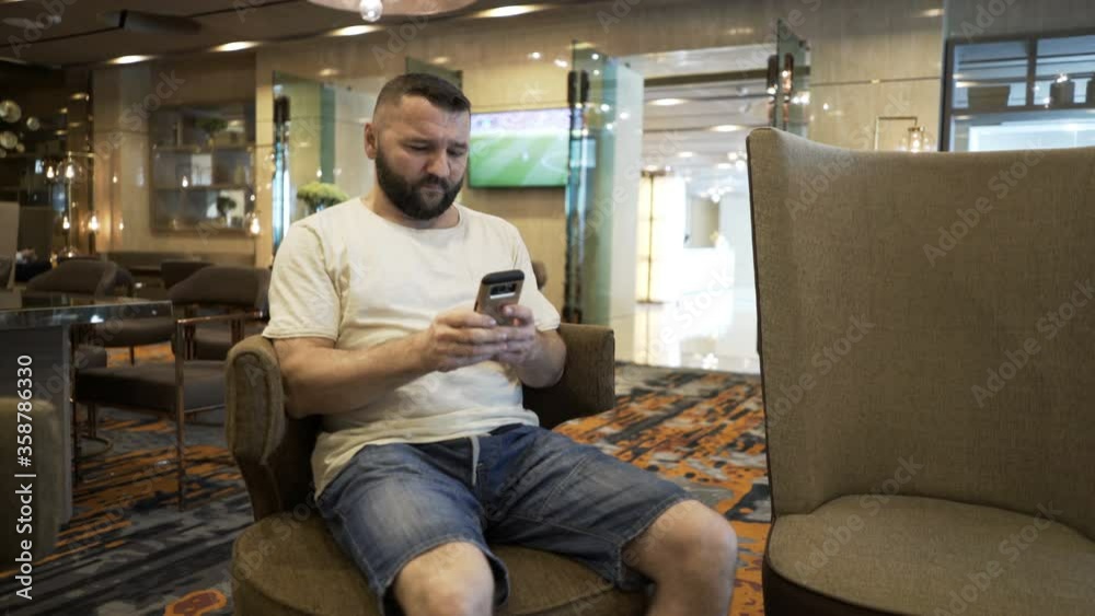 Young man texting on smartphone sitting in hotel lobby Young man texting on smartphone sitting in hotel lobby