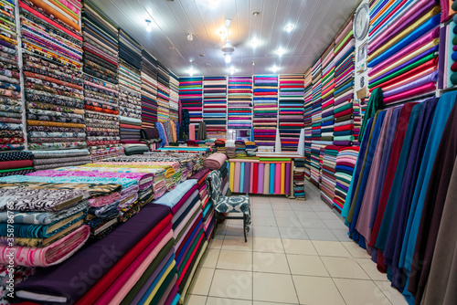 Shelf with a wide selection of colorful fabrics. Colorful ribbons on the shelf in the store. Textile industry. Clothes in shop, Rolls of fabric and textiles for sale stacked on shelves in shop. 