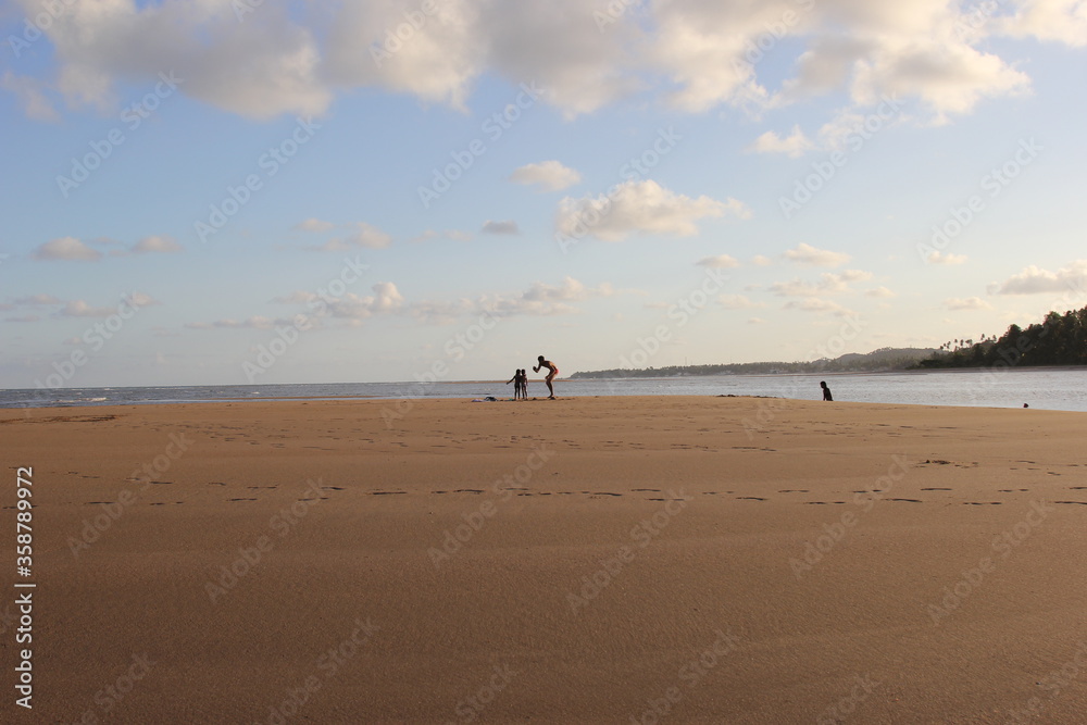 Guarajuba beach, Bahia, Brazil. Wide and open beach with beige sand at sunset. In the middle of the beach a man and two children. In the background, ocean water and vegetation. Guarajuba beach, Bahia, Brazil. Wide and open beach with beige sand at sunset. In the middle of the beach a man and two children. In the background, ocean water and vegetation.