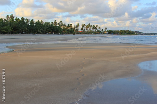 Guarajuba beach, Bahia, Brazil. Dawn with a cloudy sky over the calm waters of the ocean. In the foreground wide open beach. In the background vegetation. 