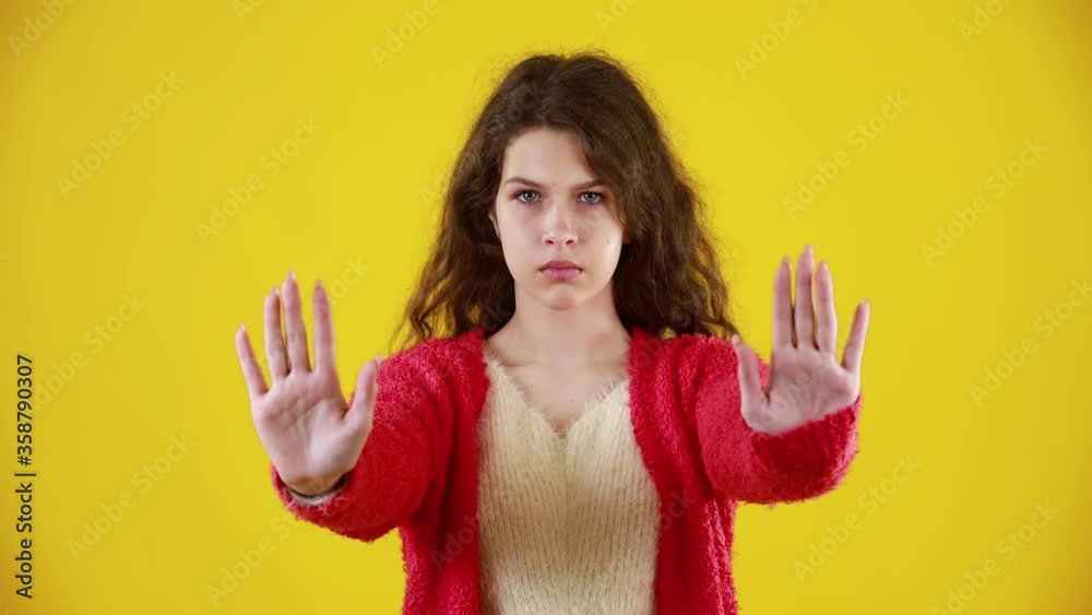 Serious attractive young woman with long wavy hair showing stop gesture with palm. Portrait of young successful confident girl isolated on yellow background. Concept of defense and lifestyle. Serious attractive young woman with long wavy hair showing stop gesture with palm. Portrait of young successful confident girl isolated on yellow background. Concept of defense and lifestyle.