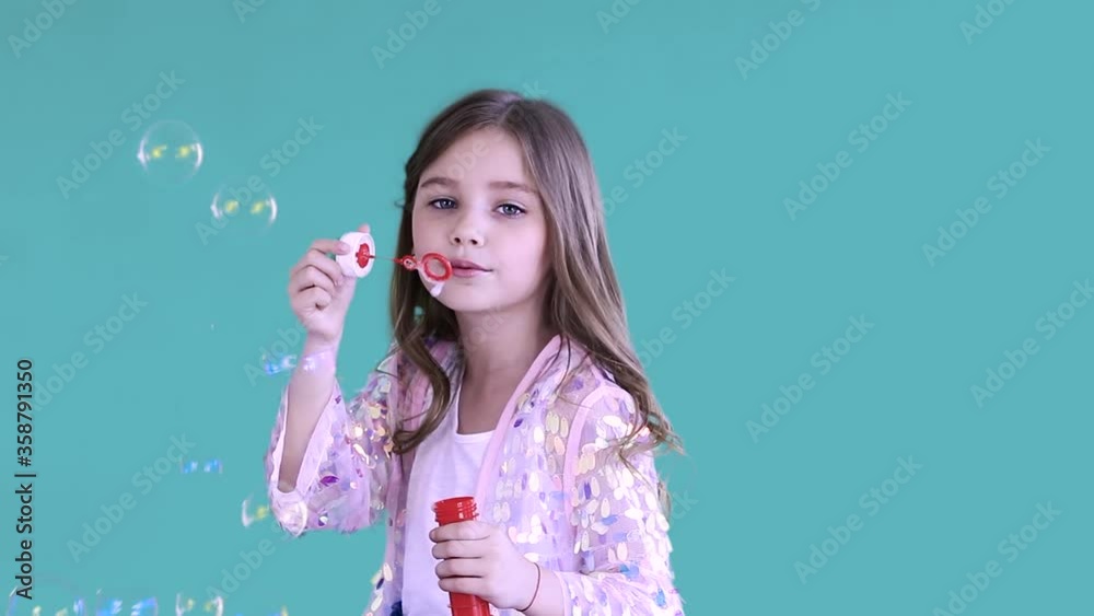 Smiling happy joyful girl in pink jacket blows the soap bubbles, looks at camera and enjoys the moment. Concept of childhood and lifestyle. Smiling happy joyful girl in pink jacket blows the soap bubbles, looks at camera and enjoys the moment. Concept of childhood and lifestyle.