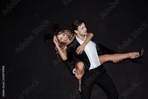 Attractive girl in bunny ears laughing while piggybacking on man in suit isolated on black