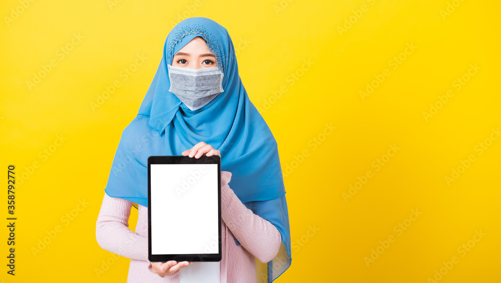 Asian Muslim Arab, Portrait of happy beautiful young woman Islam religious wear veil hijab and face mask protect quarantines disease coronavirus show blank screen tablet isolated yellow background Asian Muslim Arab, Portrait of happy beautiful young woman Islam religious wear veil hijab and face mask protect quarantines disease coronavirus show blank screen tablet isolated yellow background