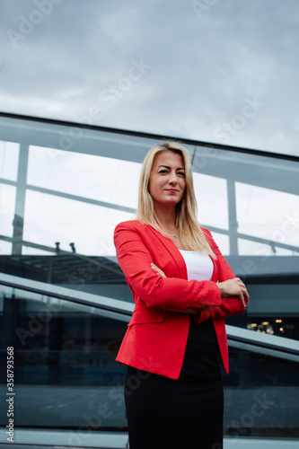 Successful businesswoman in suit standing against office building, rich luxury women in elegant clothing posing for the camera outdoors, confident female entrepreneur looking satisfied with profession photo