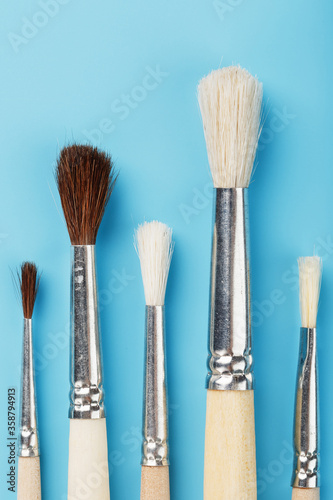 Brushes for drawing with paints made of natural wood and wool on a blue background.