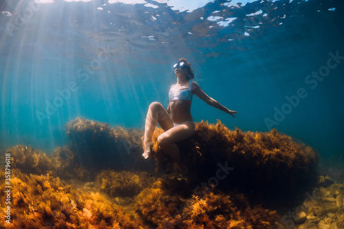 Woman freediver posing on stone with seaweed in underwater. Freediving in ocean © artifirsov