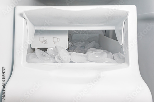 Closeup of ice maker, machine, in refrigerator with ice cubes. Concept of clean water filter, household appliance repair, maintenance and service photo