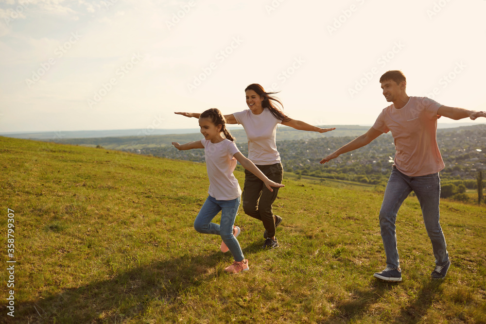A positive family cheerfully runs across the field hands to the side in the morning at dawn in the sun. A positive family cheerfully runs across the field hands to the side in the morning at dawn in the sun.