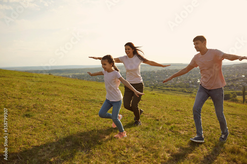 A positive family cheerfully runs across the field hands to the side in the morning at dawn in the sun.