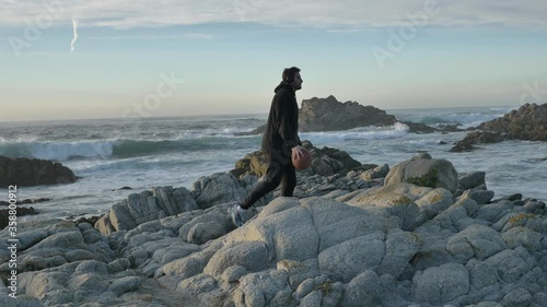 Slow motion cinematic of authentic and trendy basketball player in black sport suit practacing with ball at sunset filled california vibes on warm summer evening