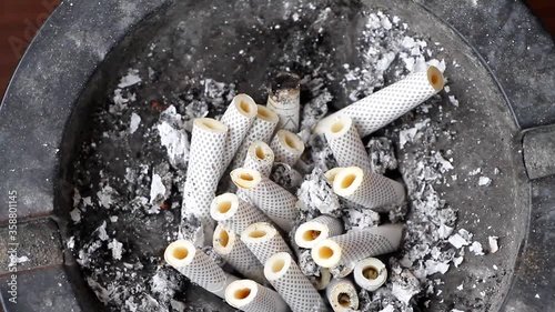 Ashtray filled with slim cigarette butts. Concept for quitting smoking, no tobacco day, quitting addiction, anti-smoking campai. Rotation 360 degrees Top view closeup. photo