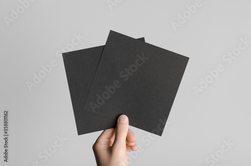 Black Square Flyer / Invitation Mock-Up - Male hands holding black flyers on a gray background.