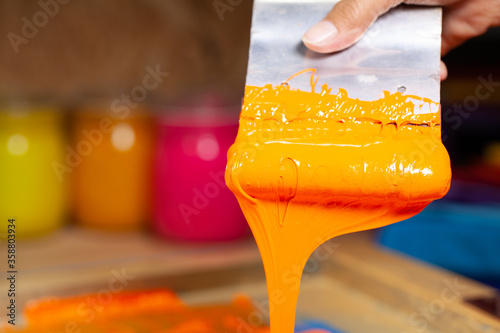 .orange color dripping from hand screen printing during printing tee shirt .in tee shirt factory. photo