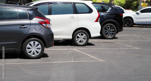 Closeup of rear, back side of black car with other cars parking in outdoor parking in bright sunny day. 