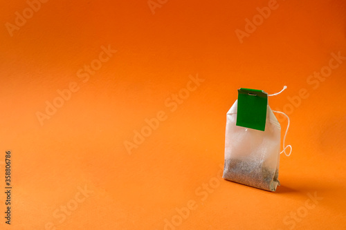 A bag of tea with a green tag and a thread on an orange background.