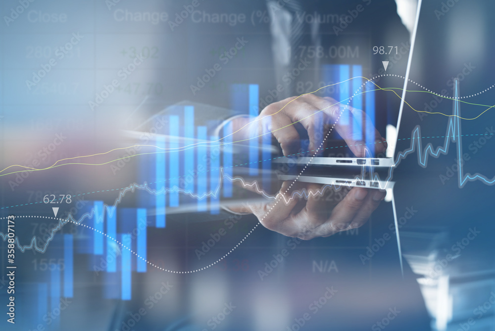 Businessman monitoring stock market report on laptop computer with financial graph on virtual screen for business analysis concept Businessman monitoring stock market report on laptop computer with financial graph on virtual screen for business analysis concept