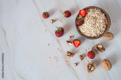 Home cooking. A healthy Breakfast of oatmeal, walnuts and fresh delicious organic strawberries on a light marble background. Top view. Free space.