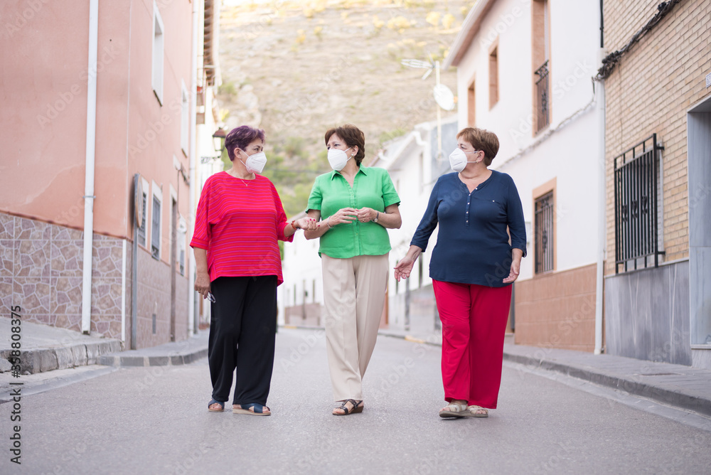 Obraz premium 3 older women with face mask on the street and one of them looking at the camera