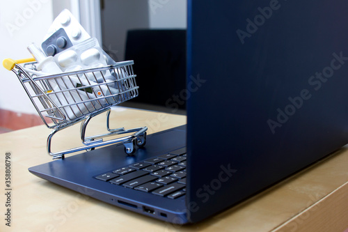 Close up Laptop and pills in small shopping trolley. Online Pharmacy. Drugs delivery. Online shopping. Stay home. Order Supplements and medications At An Online Pharmacy