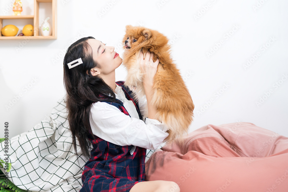 Pet lover. An Asian woman is playing with a Pomeranian dog in a living room.